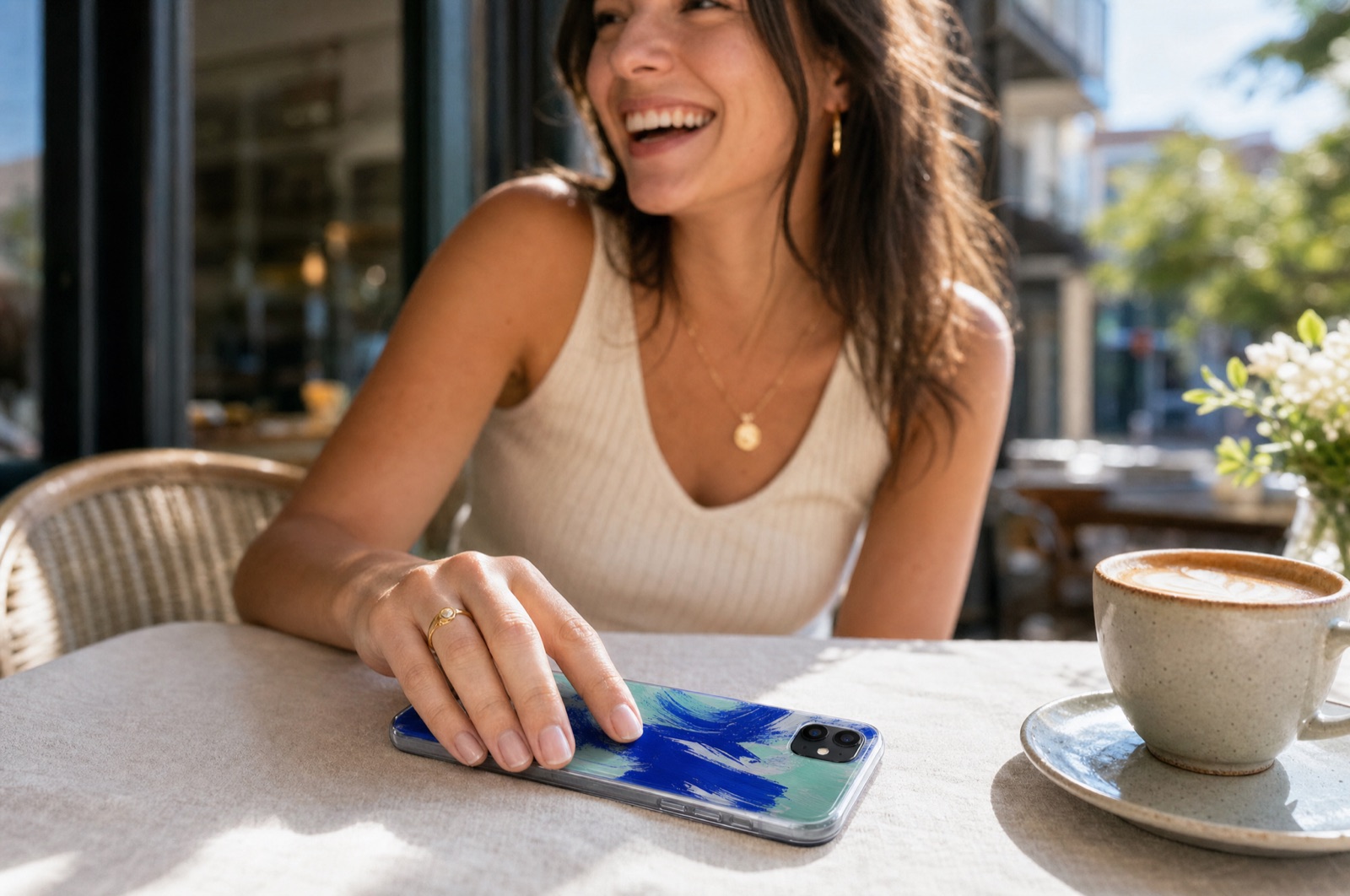 A woman laughing at a café table, her phone in a UV-printed transparent case in the foreground