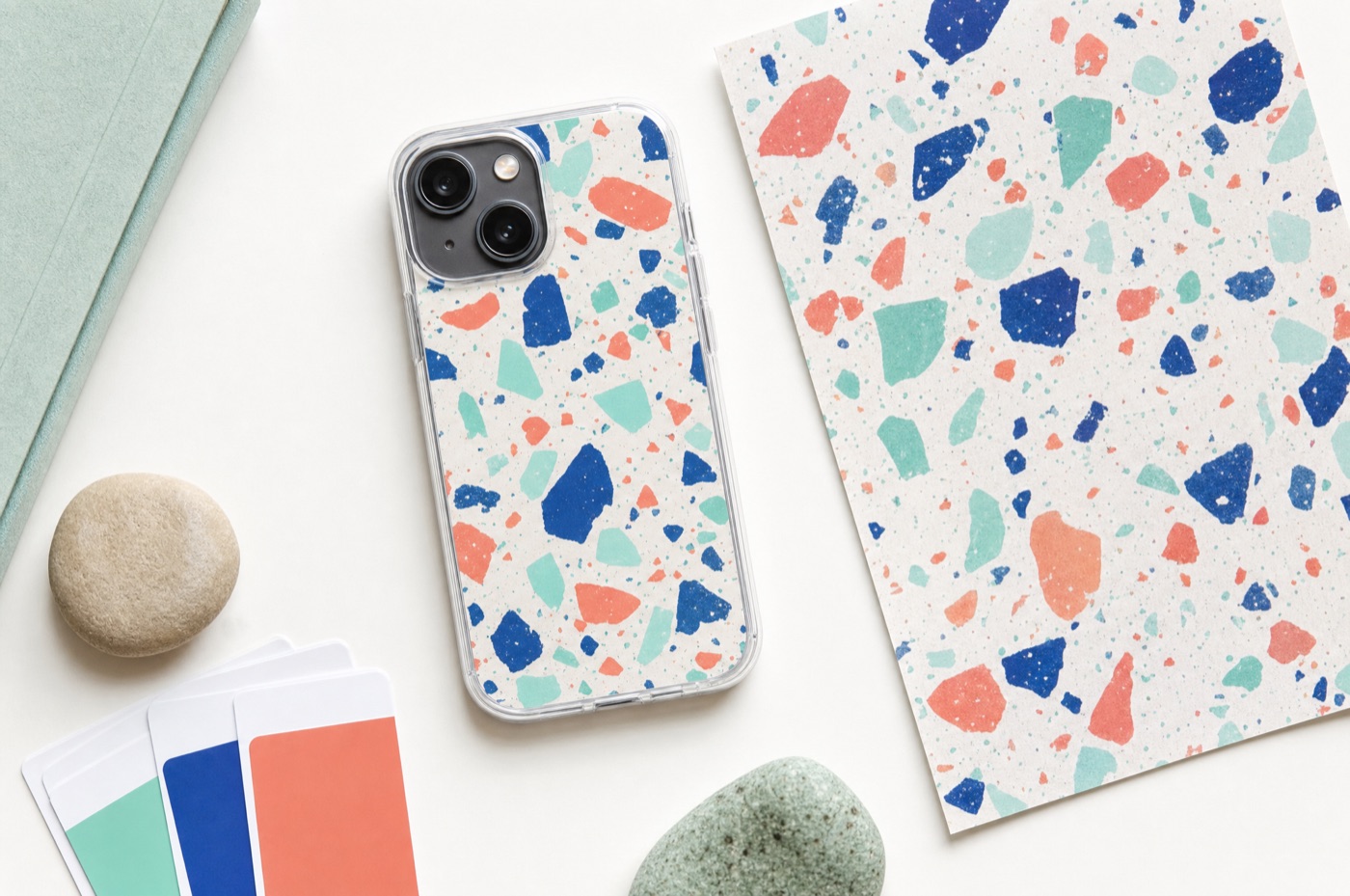 A phone in a terrazzo-printed transparent case beside the printed artwork sheet